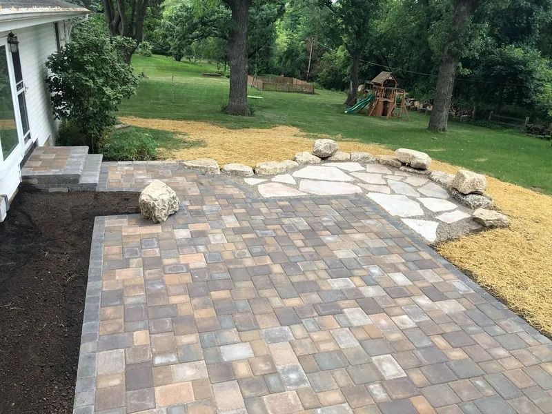 Backyard patio with gray pavers, stepping stones, rocks, and lawn beside a house