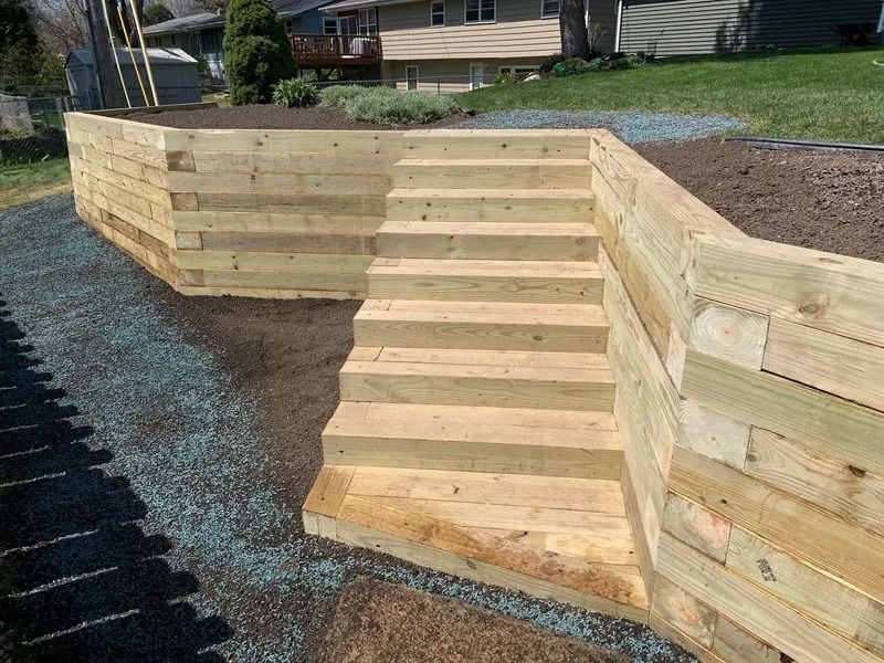 Wooden outdoor steps leading to a raised garden bed wall on a landscaped slope.