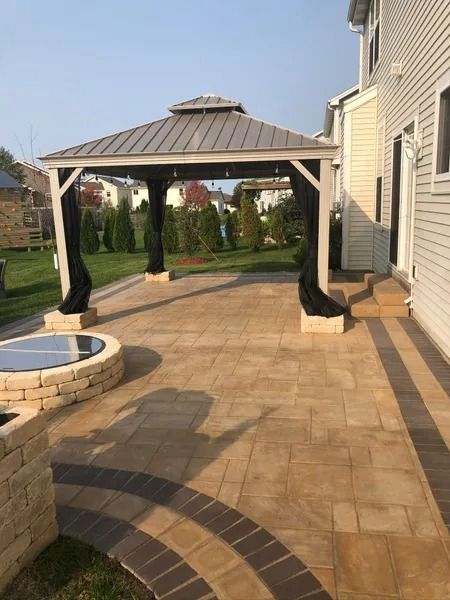 Backyard stone patio with a gazebo beside a house and a small fire pit.
