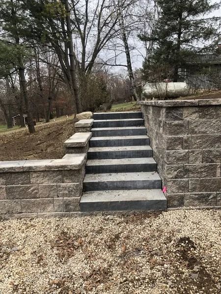 Outdoor stone staircase with retaining walls and leafless trees in the background.