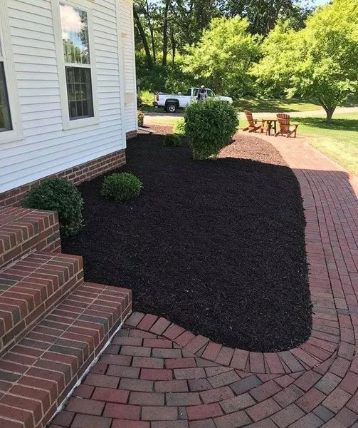Front yard landscaping with black mulch, brick walkway, steps, and a house beside a grassy yard.