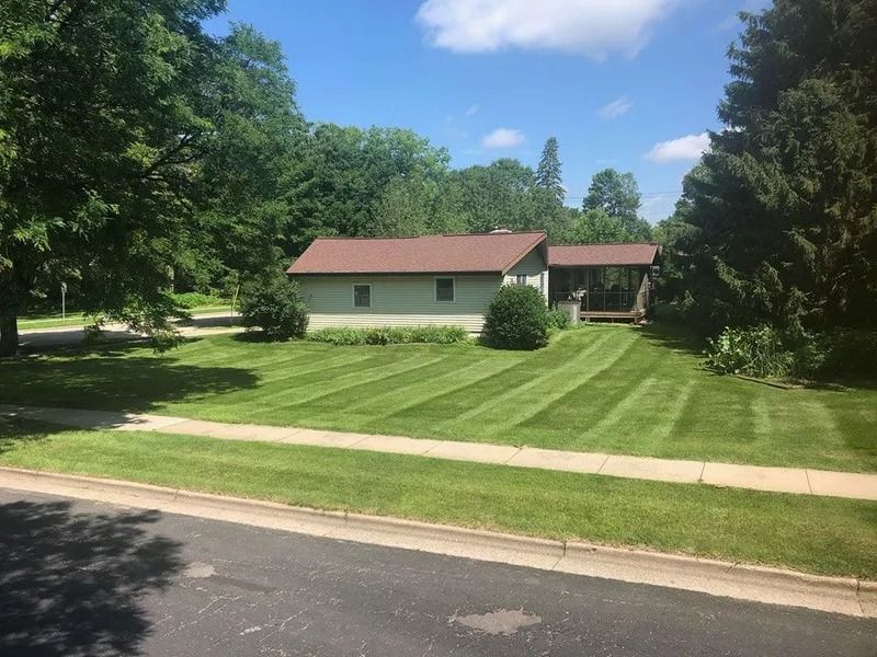 Suburban house with a red roof, neatly mowed lawn, trees, and a quiet street in front.