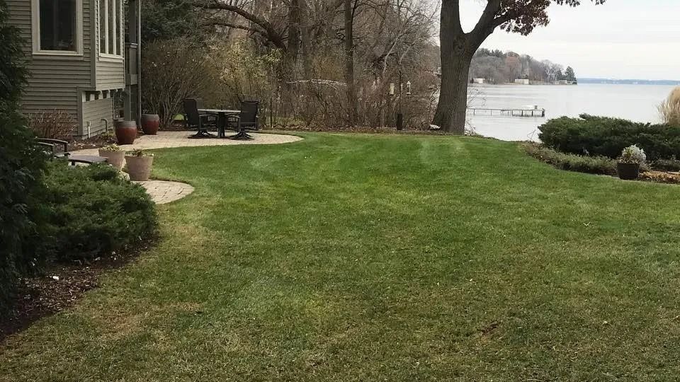 Front yard lawn beside a house, with shrubs, patio chairs, and a lake view in the distance