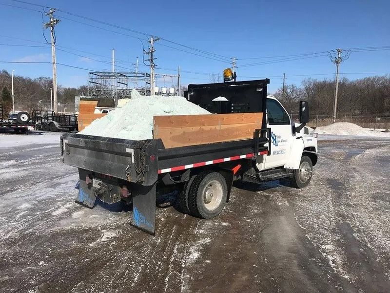White dump truck loaded with snow or gravel in an icy parking lot under a clear blue sky