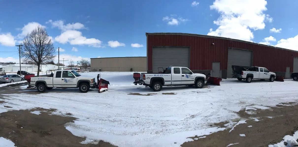 Snowy parking lot with three pickup trucks beside a large red building under a blue sky