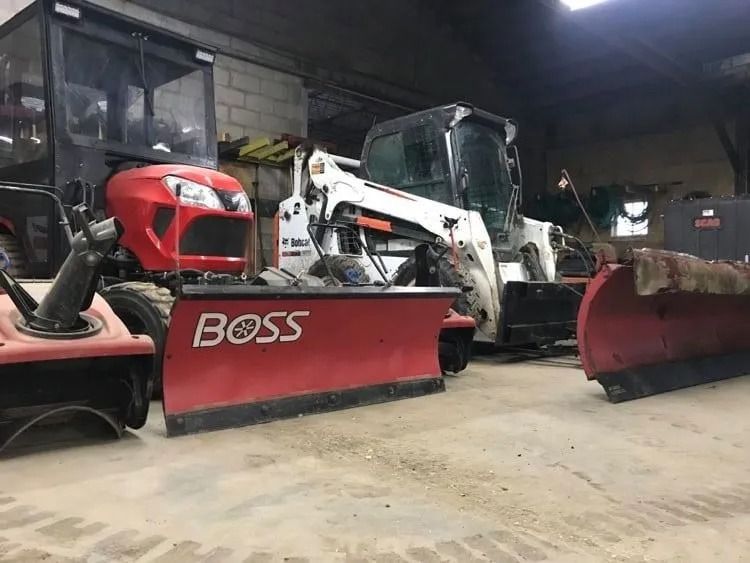 Row of red and white snowplows and skid steers inside a dim equipment garage