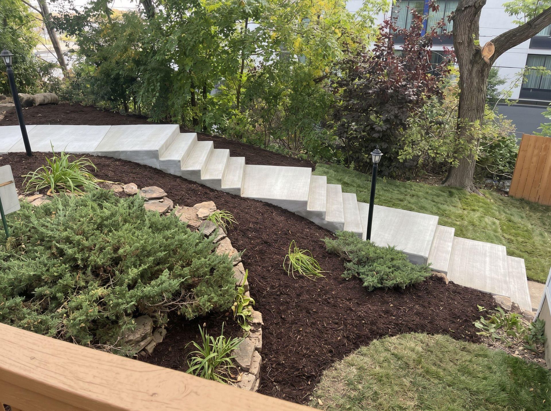Backyard stone steps leading to a raised patio, bordered by green lawn and shrubs