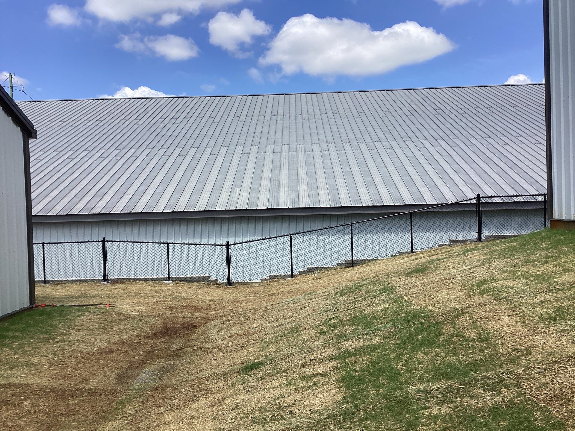 A large white barn with a metal roof on a grassy hill under a partly cloudy sky.