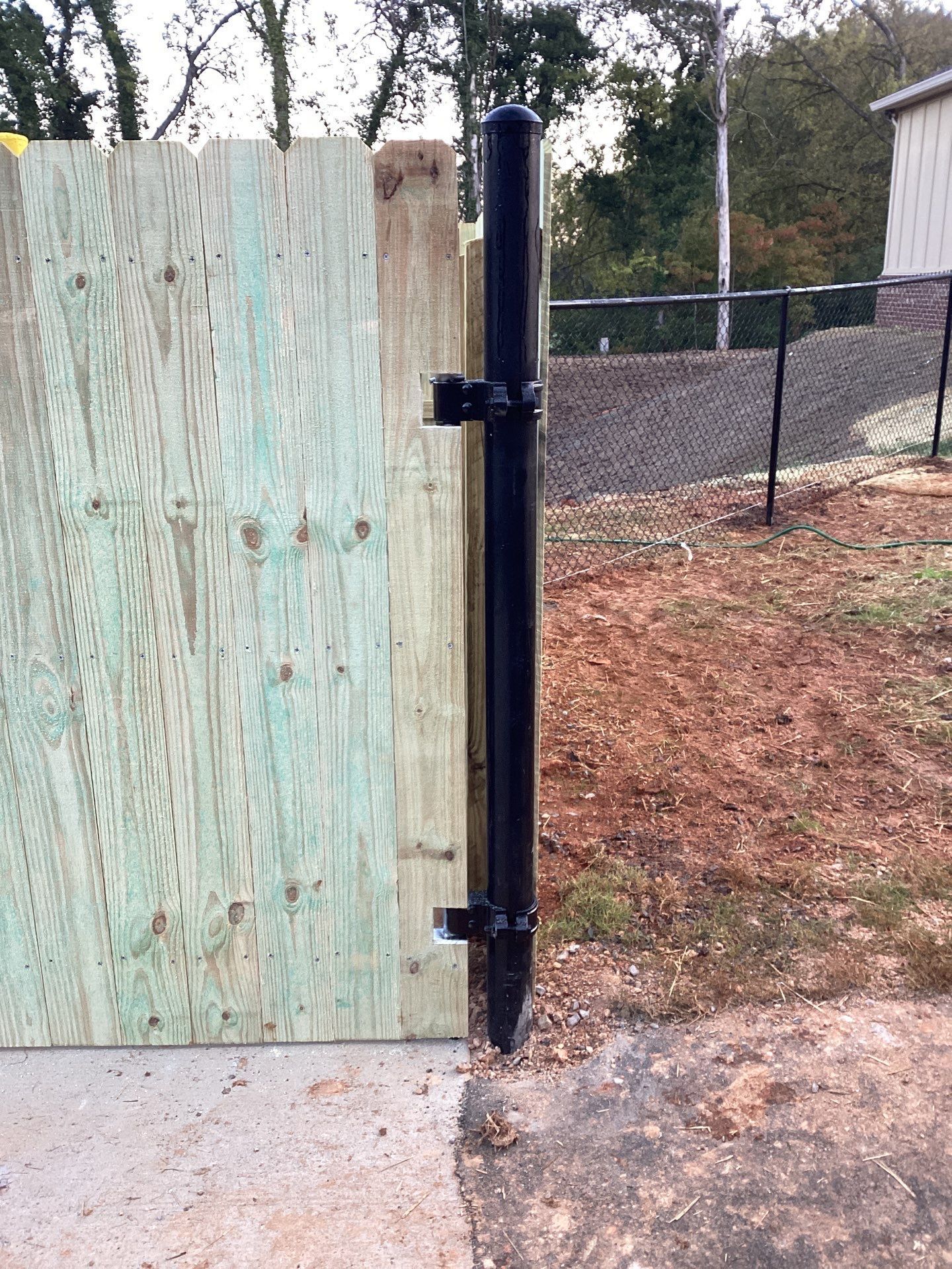 Black metal gate post with a latch, next to a wooden fence.