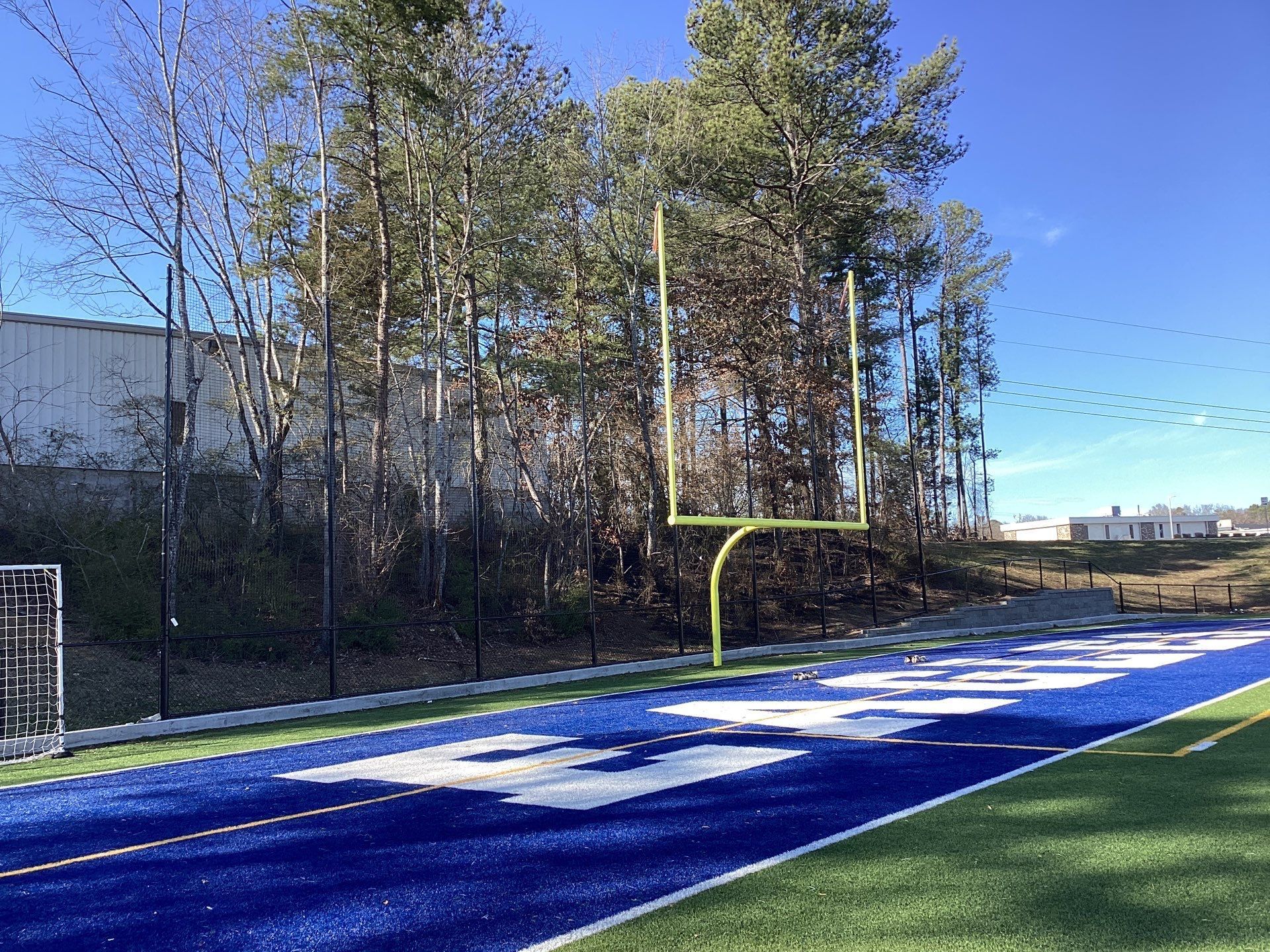 Football field with blue end zone, gold goalpost, and trees under a clear sky.