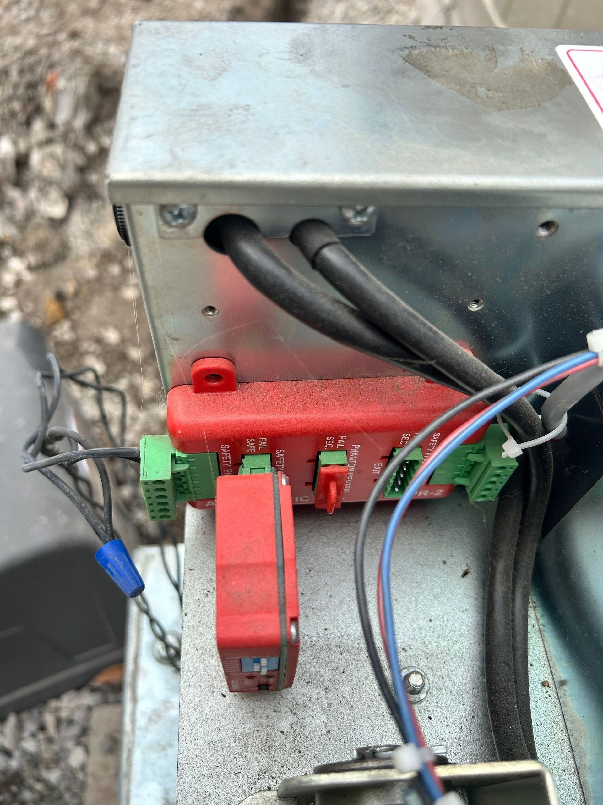 Metal box with wires and red control modules. Two black cables enter the box.