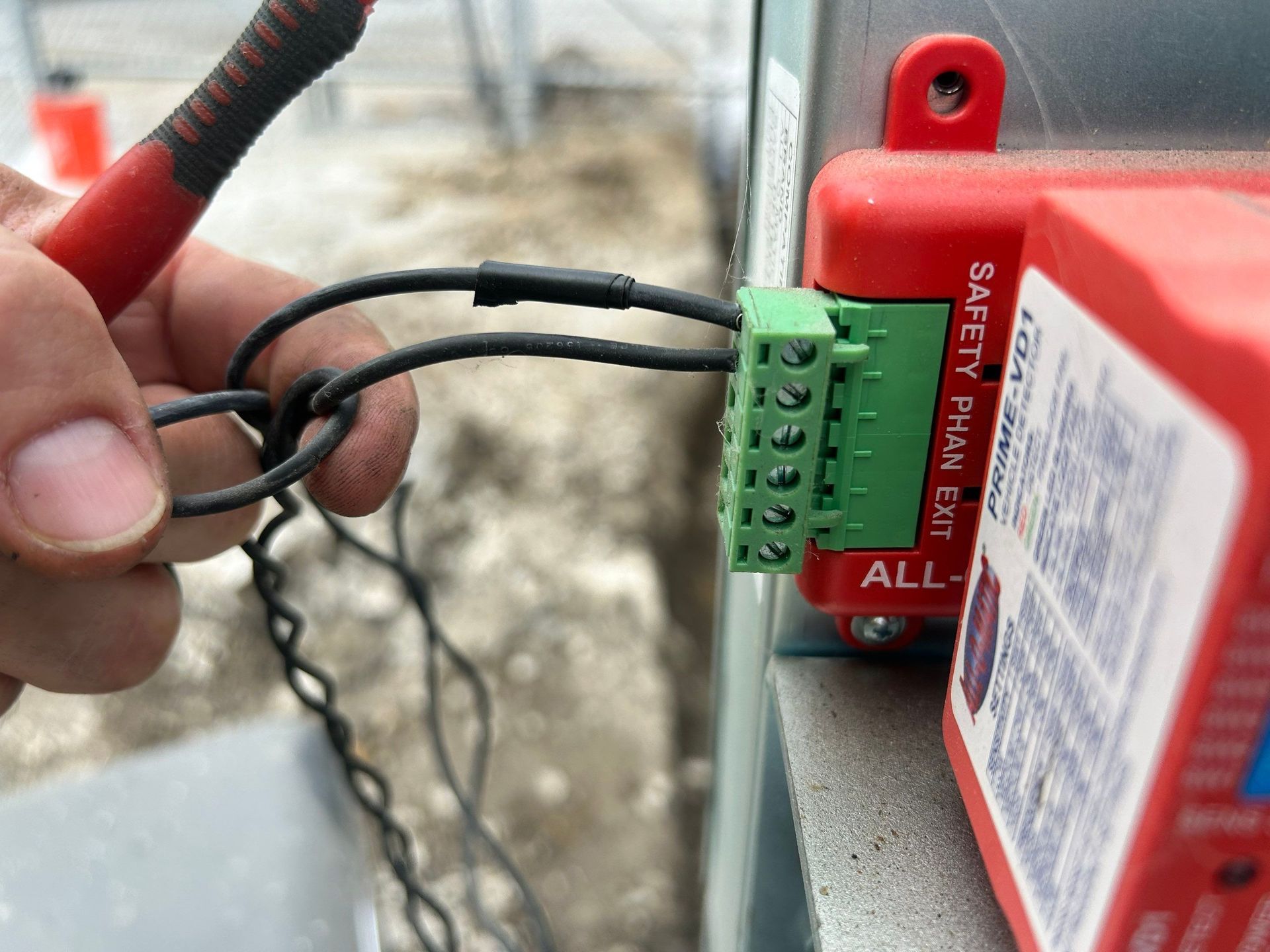 Hand holding black wires connected to a green terminal block on a red electrical box.