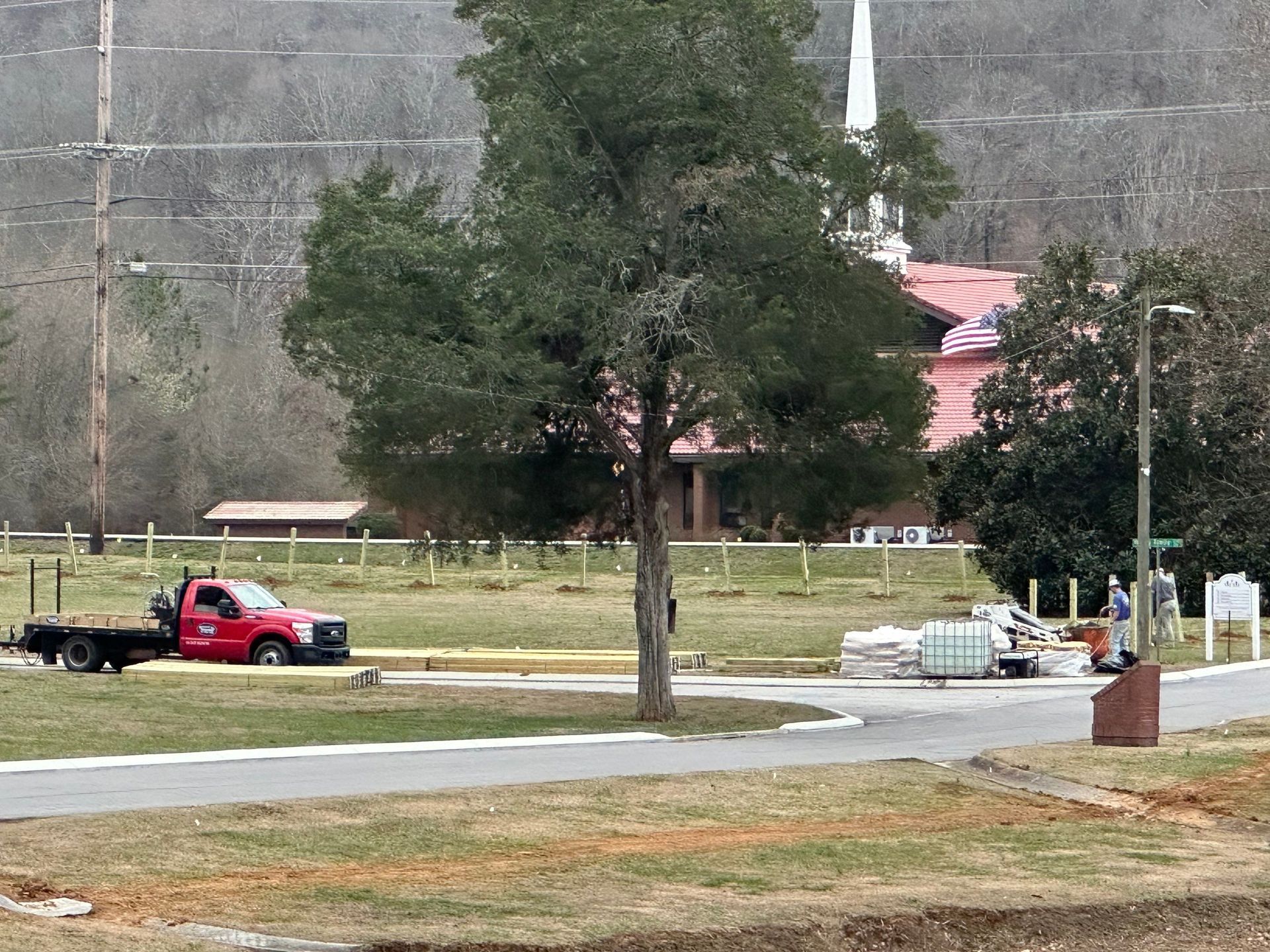 Red truck parked near a building with a white steeple. Construction materials on the ground.