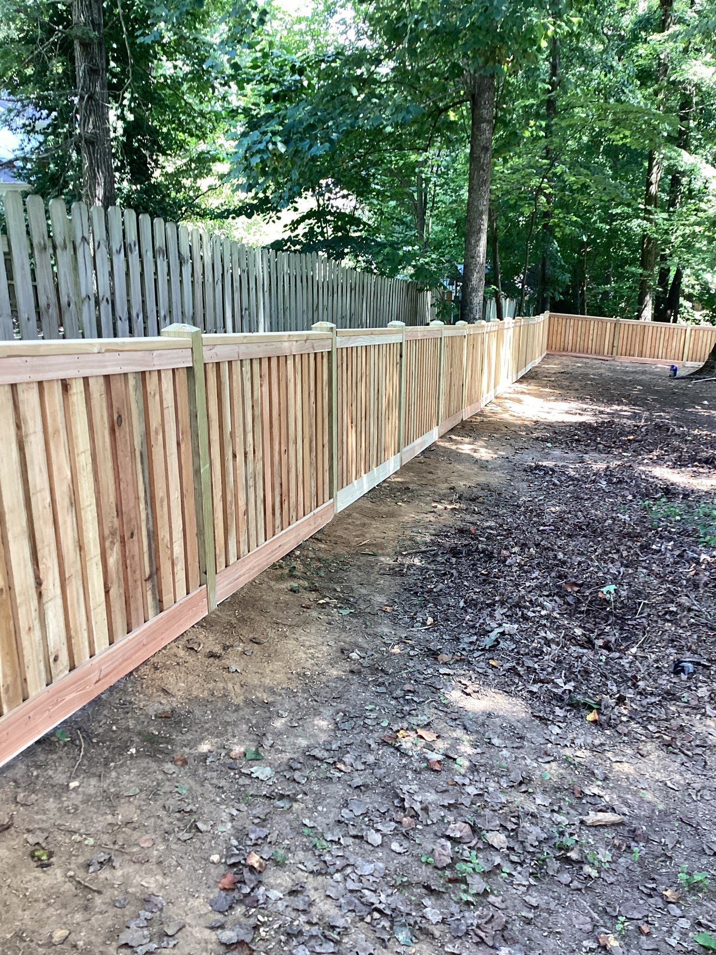 Wooden fence in a backyard, brown and natural tones, on dirt ground, trees in the background.