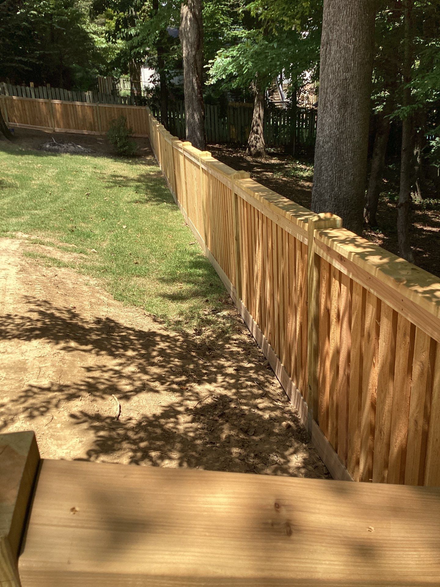Wooden fence along a grassy yard with trees, sunny outdoor setting.