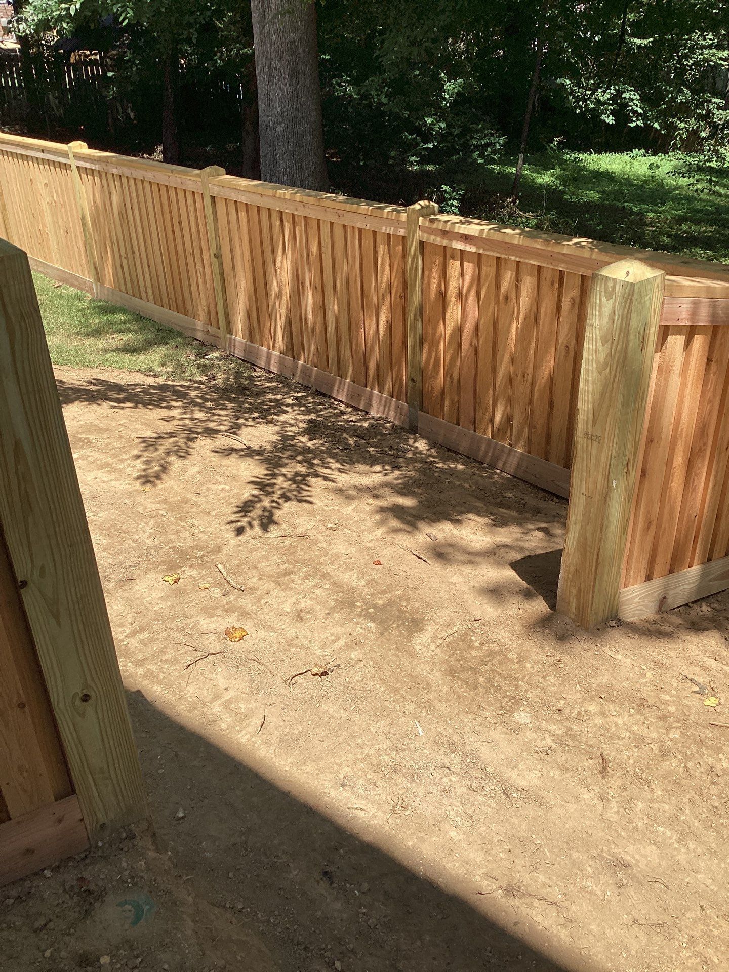 Wooden fence extending along a dirt path, with trees in the background under a sunny sky.
