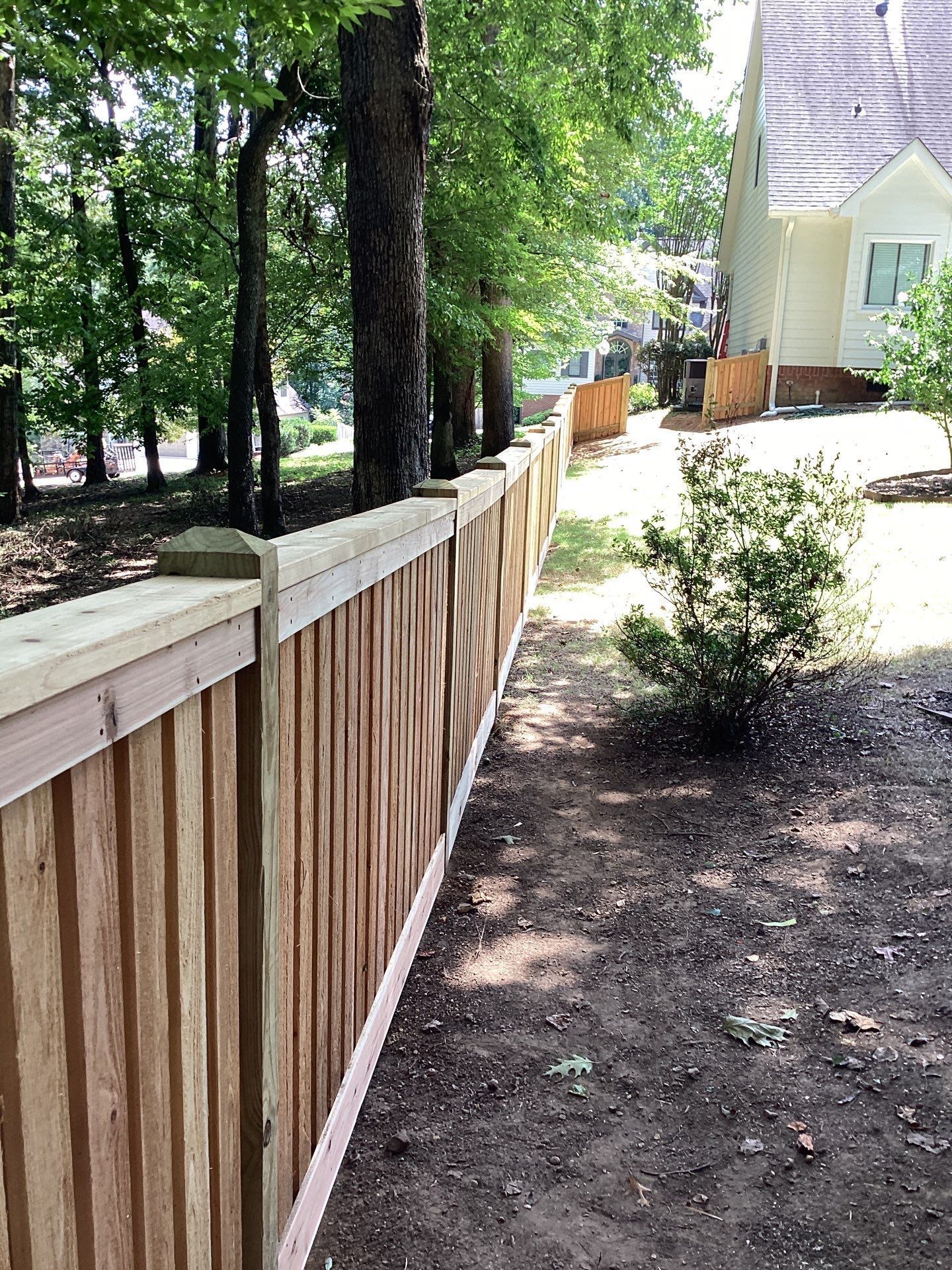 Wooden fence in a yard, trees and house in the background. Brown wood with a light top rail.