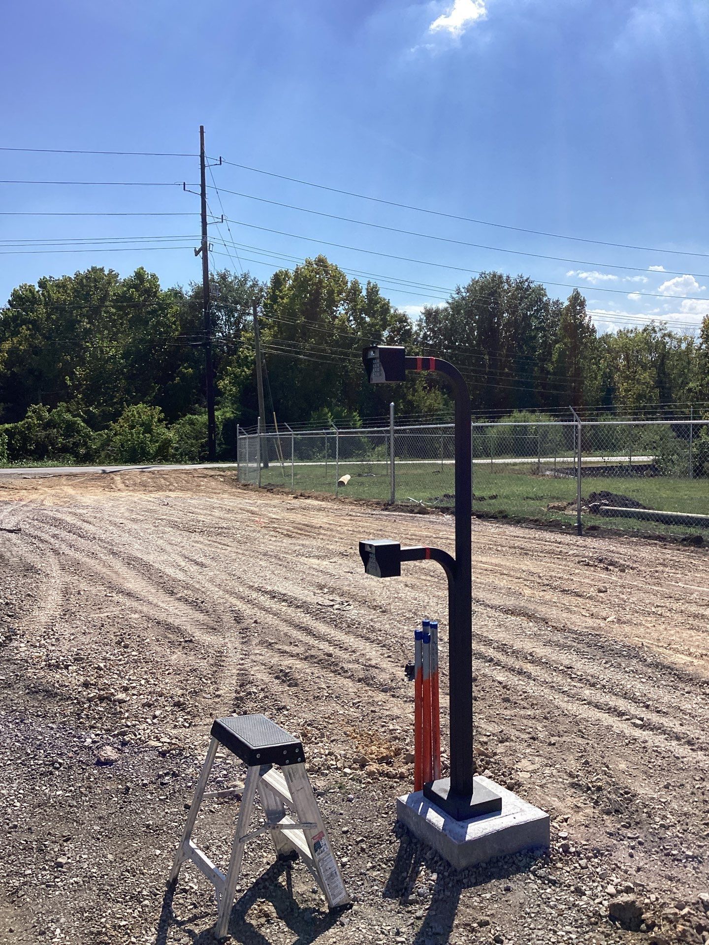 A black pole with attached equipment stands on a concrete base. A small step stool is nearby on a gravel area.