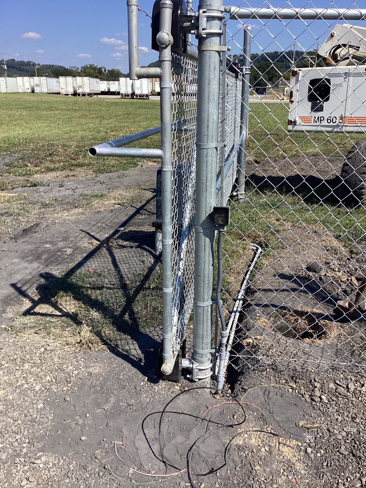 Chain-link fence gate, partially open, with ground and utility truck in the background.