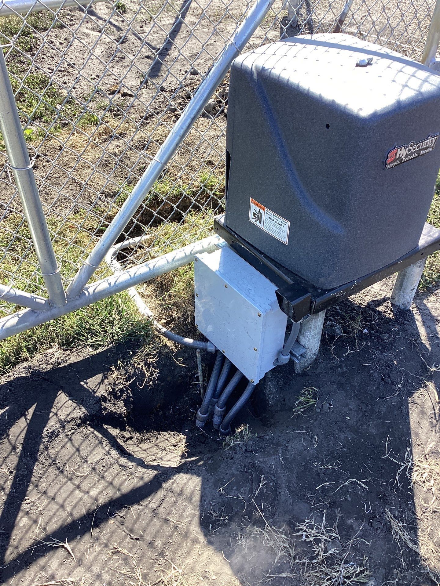 Automatic gate opener attached to a metal fence; gray box and dark motor housing.