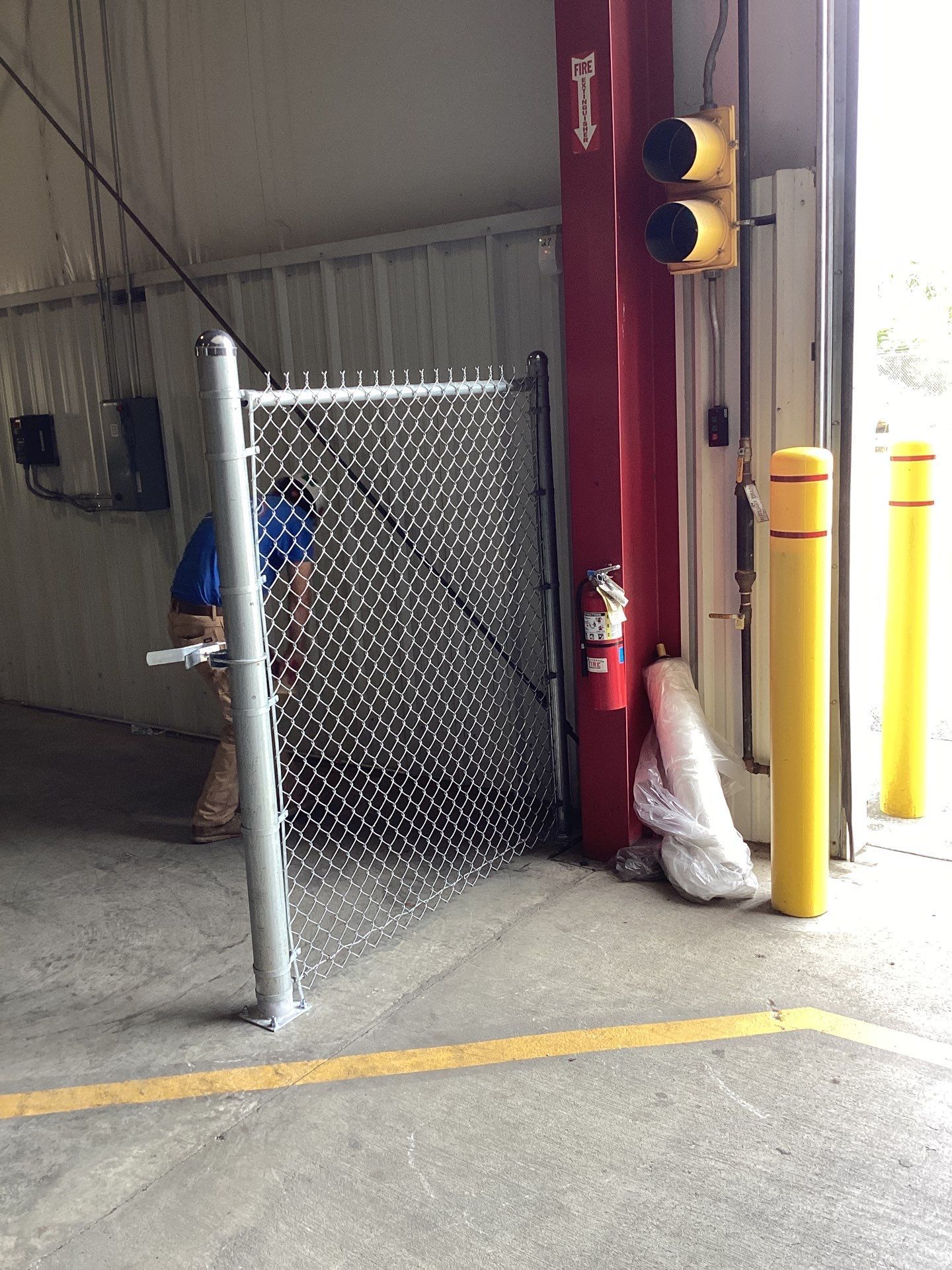 Chain link gate open in an industrial setting. Yellow poles and traffic lights.