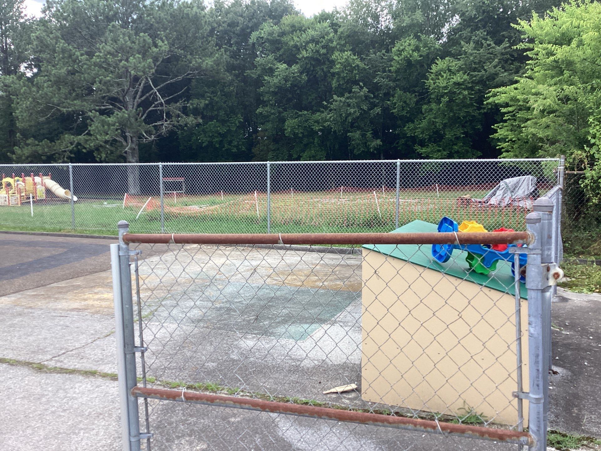 Chain-link fence with gate, leading to a grassy area with trees and a small play structure.