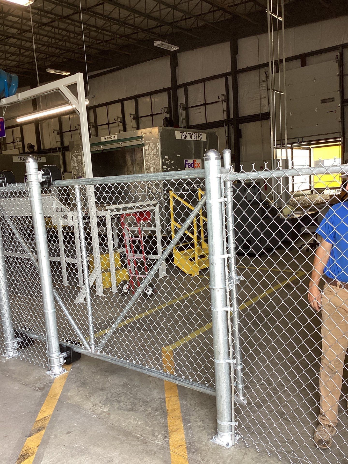 Chain-link fence with a gate in an industrial setting. A person stands nearby.