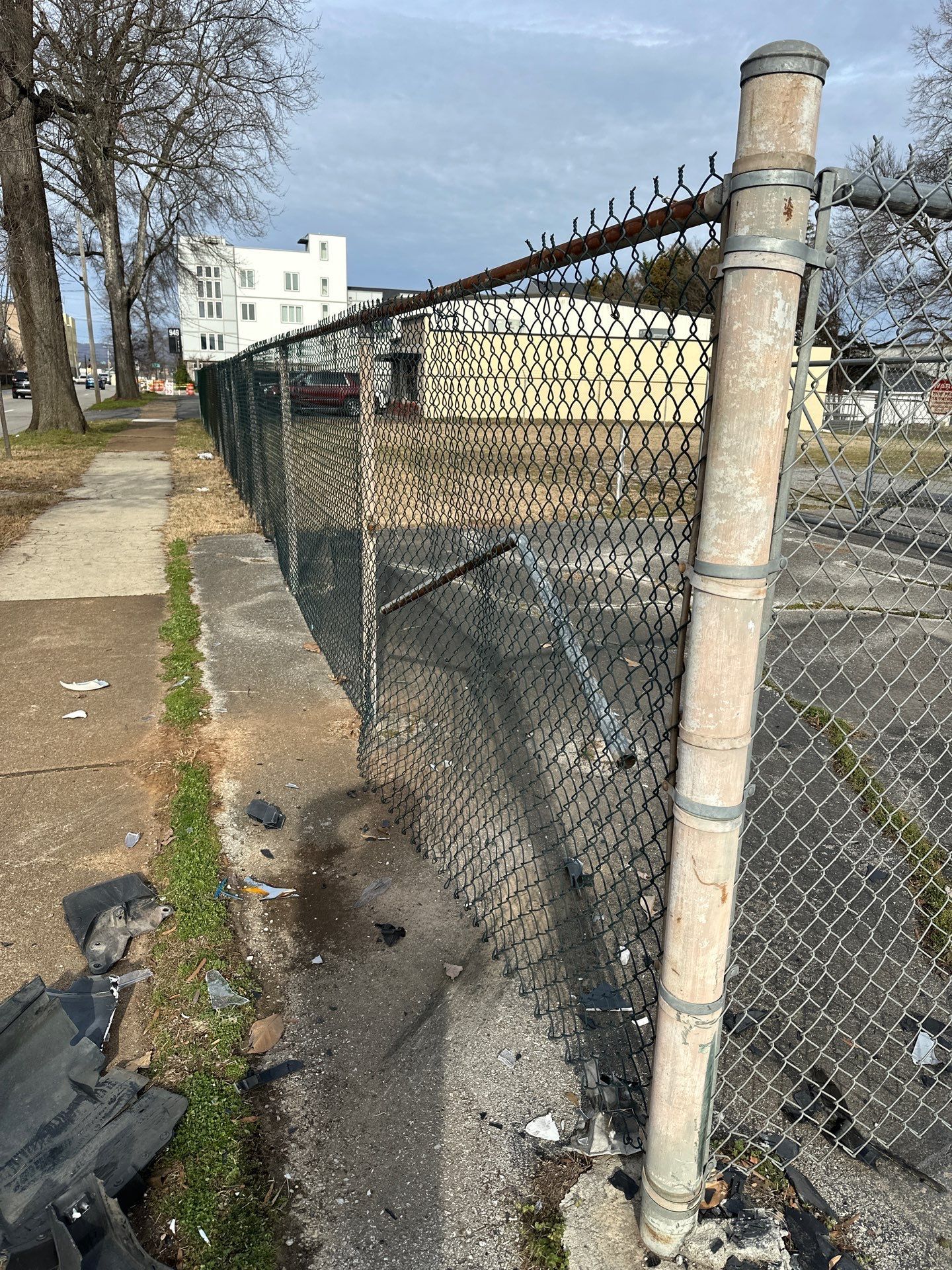 Chain-link fence with barbed wire along a sidewalk. Gray pavement and building in the background.