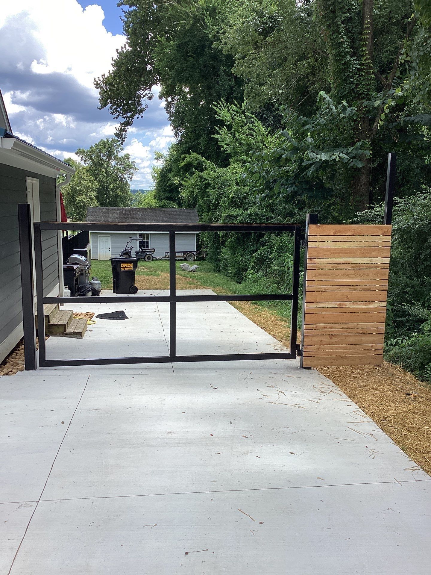 Concrete driveway with black metal gate and wooden fence on the side.