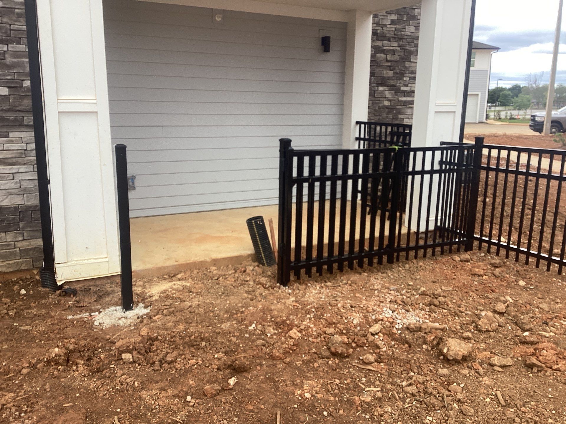 Black metal fence surrounds a concrete landing in front of a gray garage door. Brown dirt surrounds it.