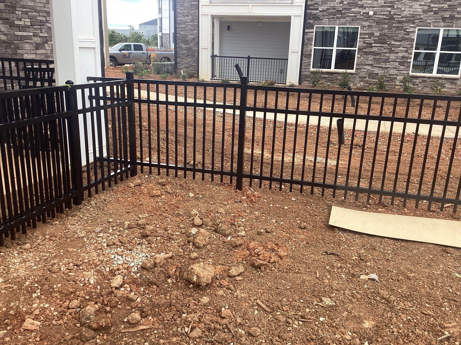 Black metal fence in front of a building with stone facade, on a patch of dirt and debris.
