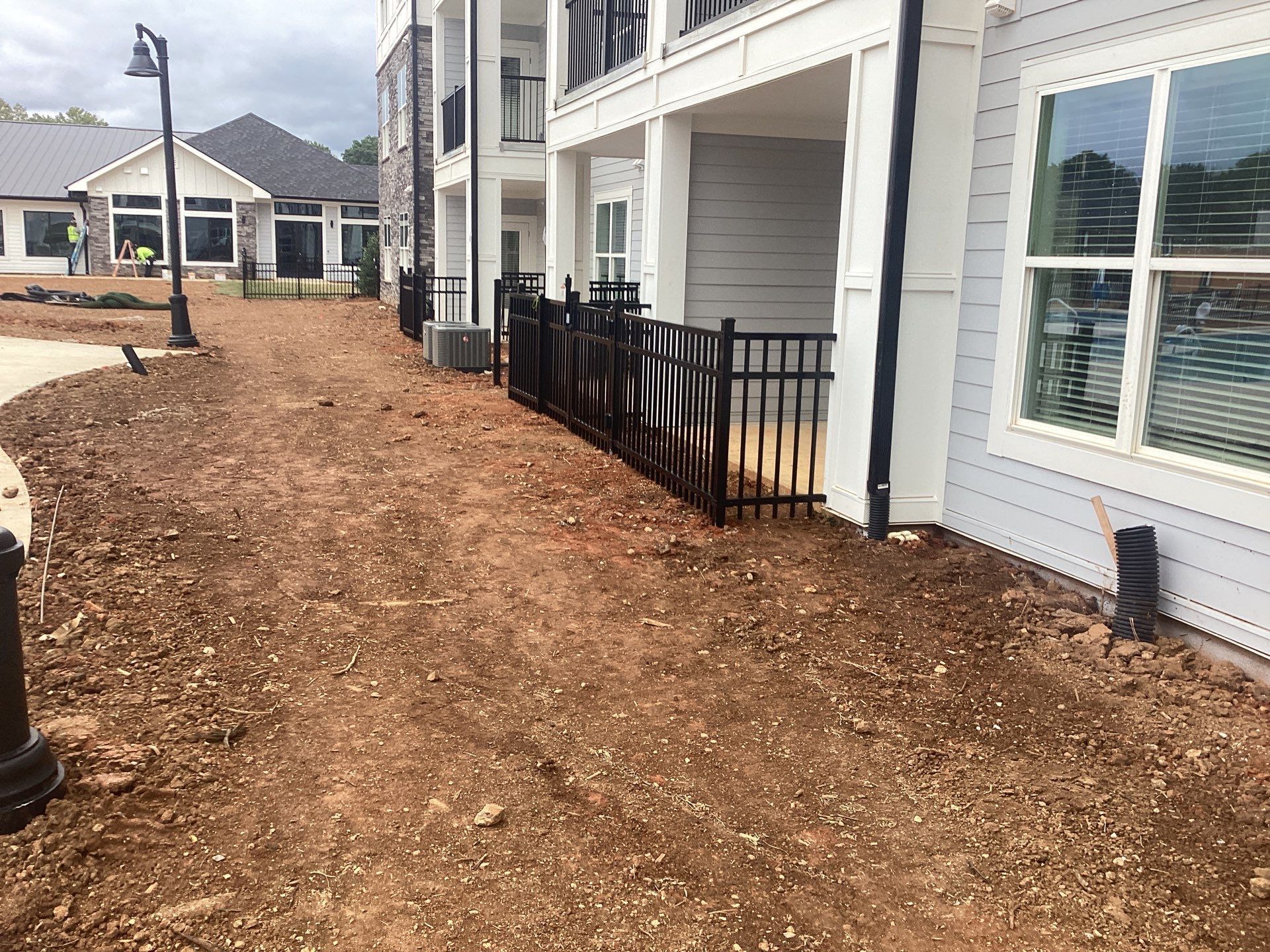 Exterior of a light blue apartment building, with a black fence and dirt ground.