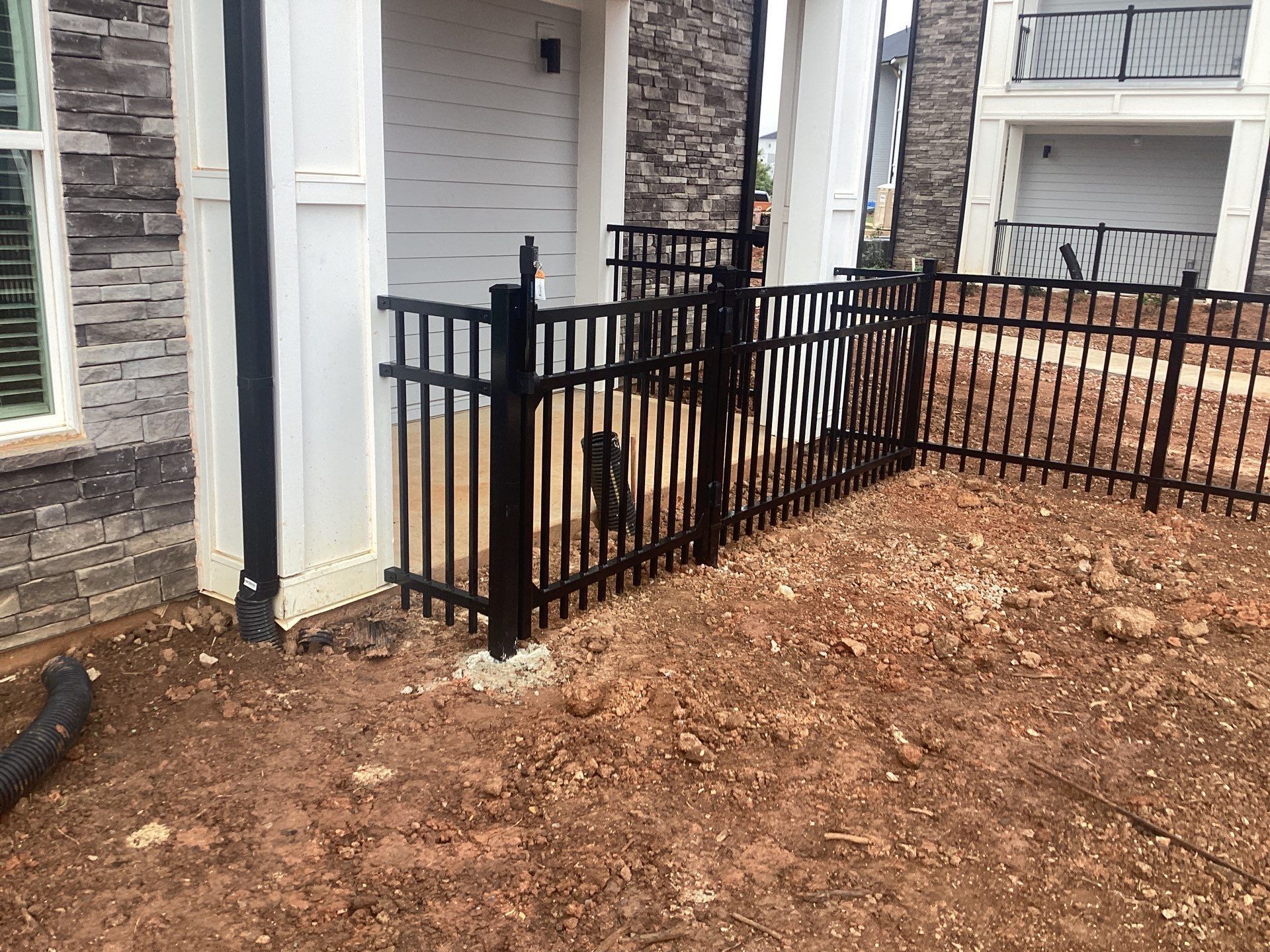Black metal fence installed on brown dirt, near a building's entrance.