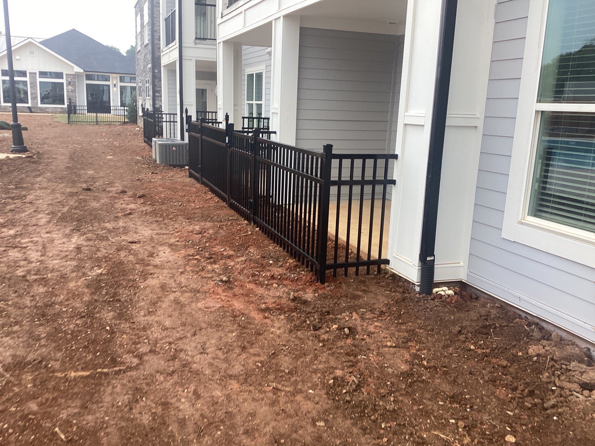 Black metal fence along an apartment building on a dirt lot.