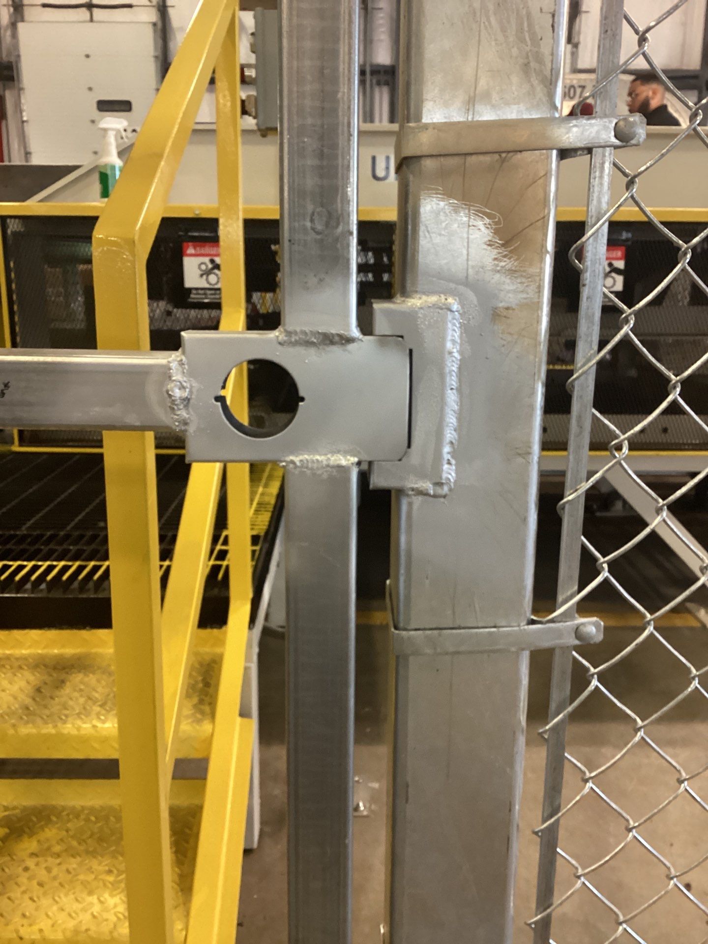 Galvanized metal gate latching to a post on a chain-link fence, near yellow stairs and metal railing.