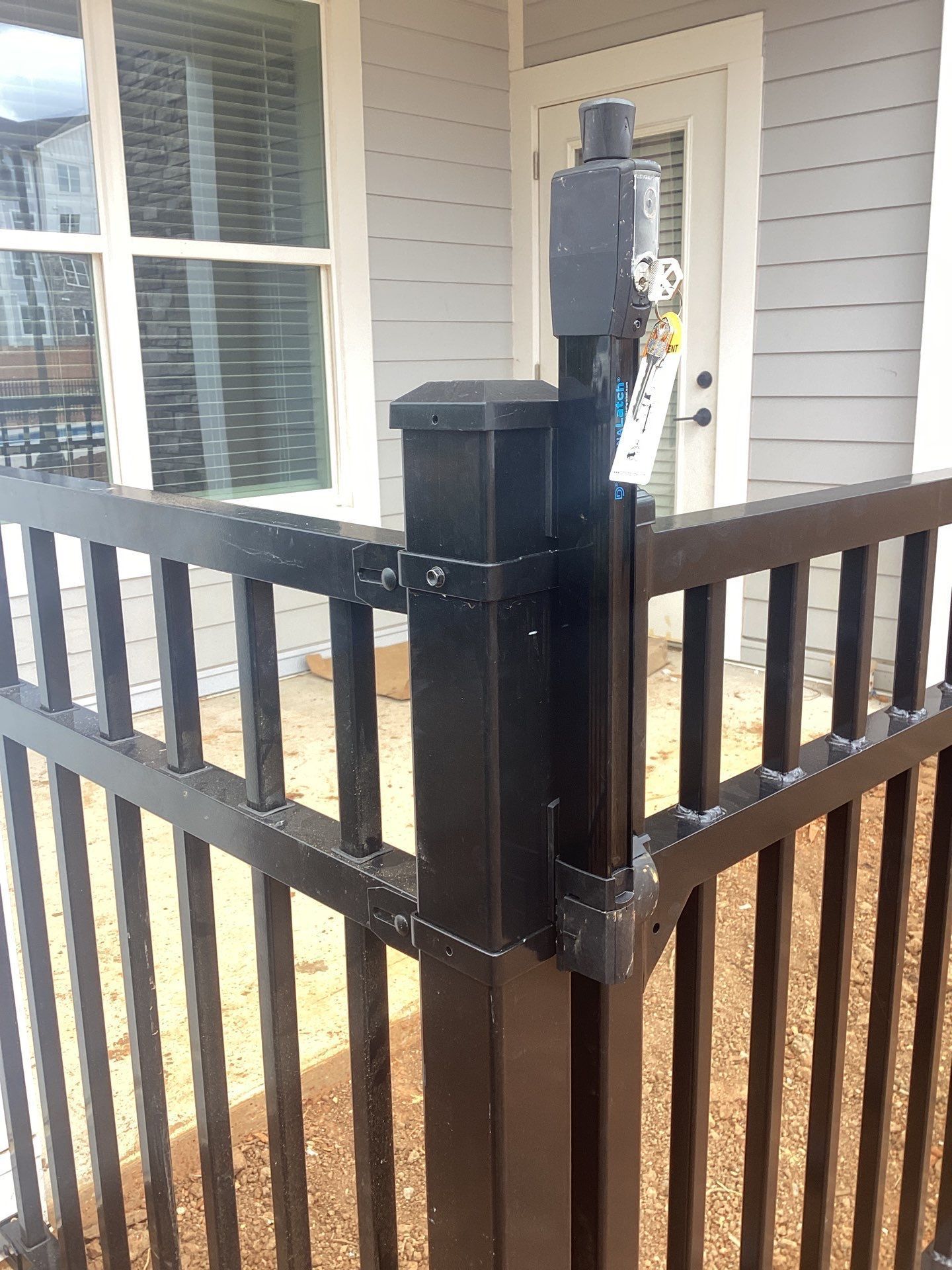 Black metal fence corner with a gate latch attached to a post, in front of a building.
