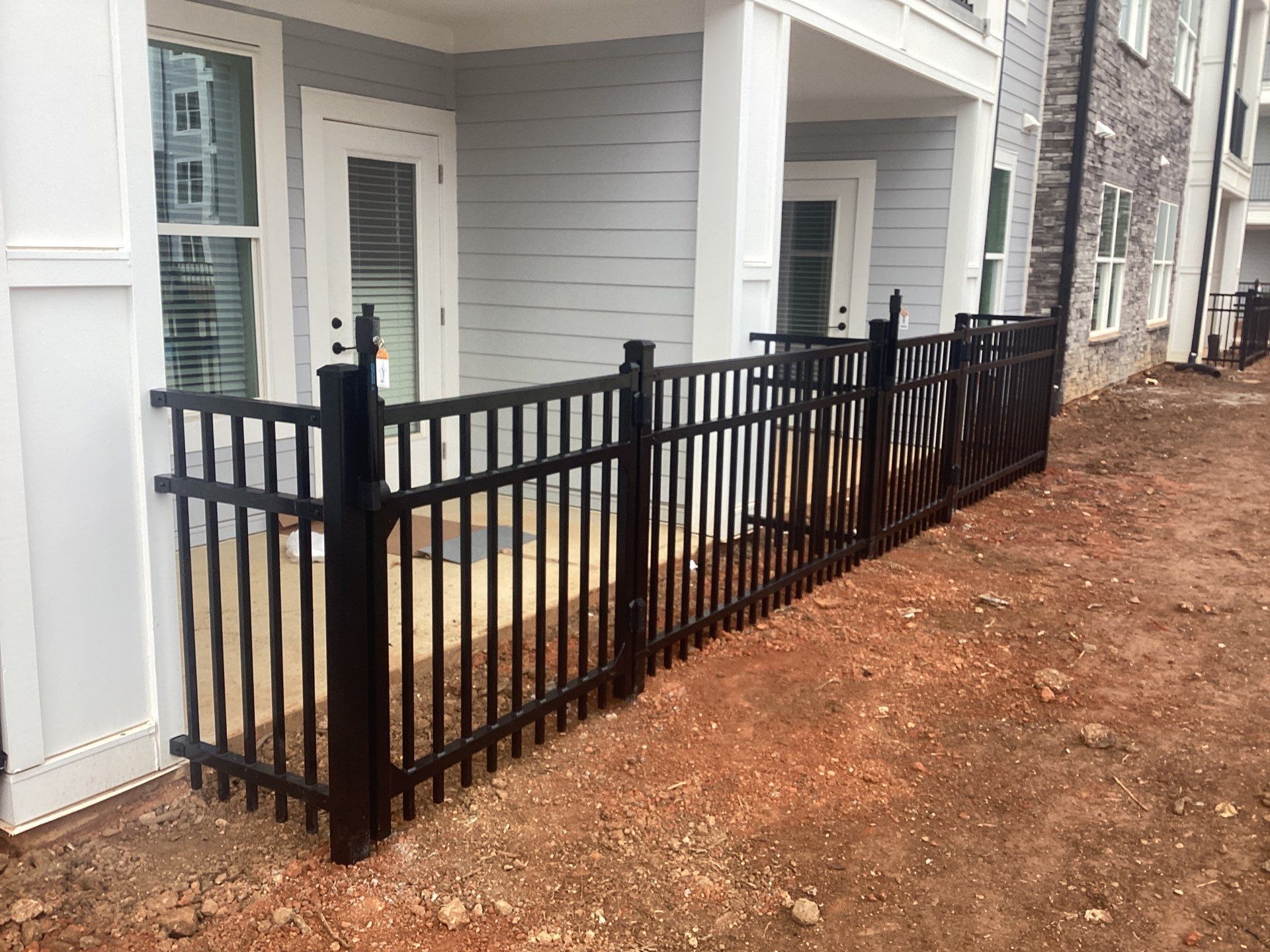 Black metal fence surrounding a patio area in front of a building with light gray siding.