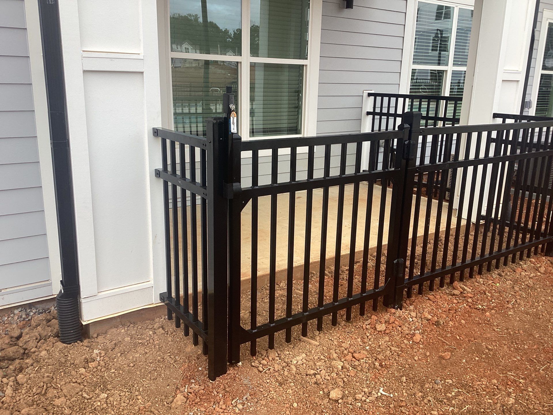 Black metal fence encloses a small patio area next to a building with white siding.