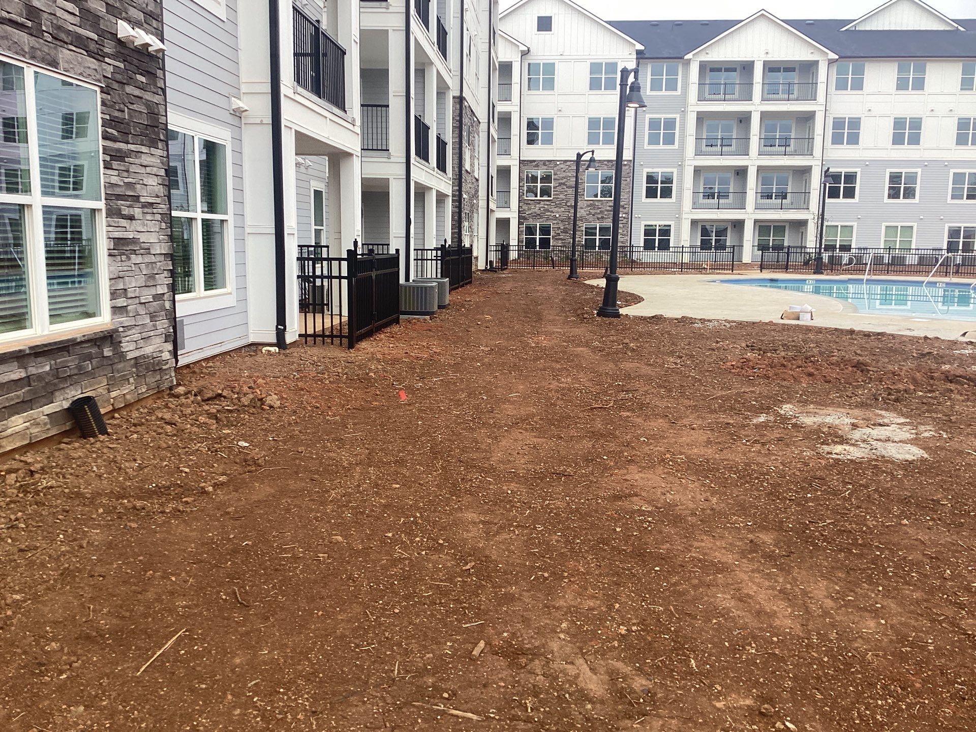 Dirt pathway next to apartment buildings and a swimming pool.