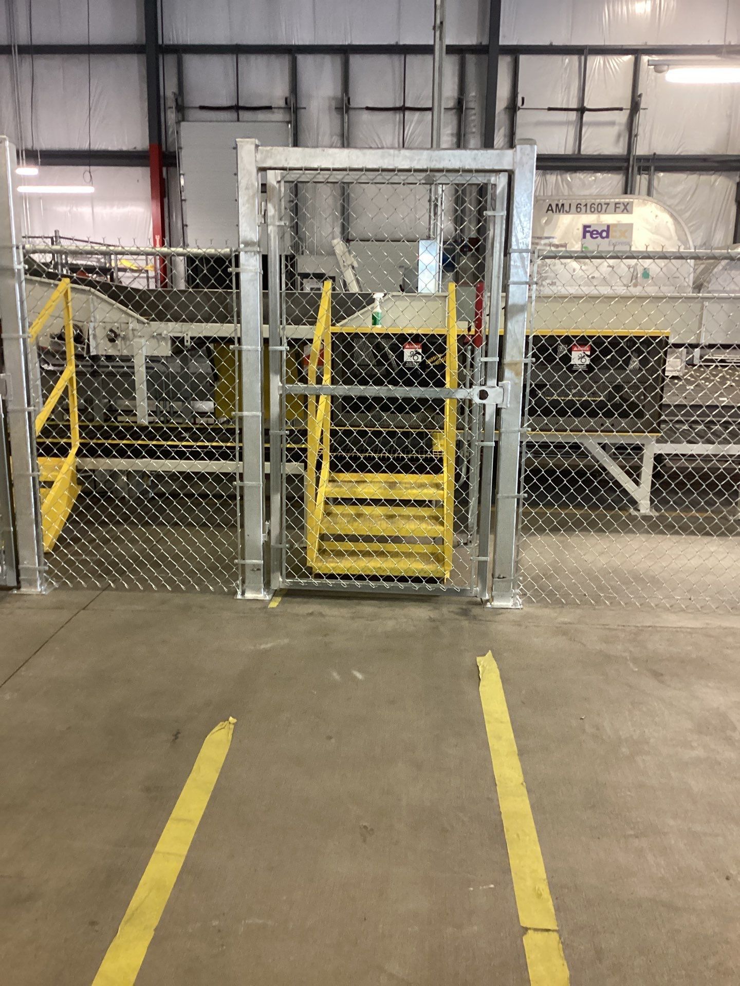 Yellow stairs inside a chain-link fence door. Yellow lines guide the floor. Industrial setting.