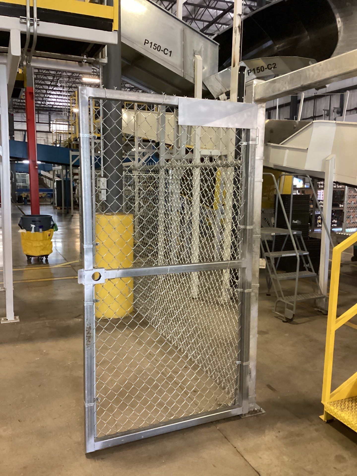 Chain-link gate, aluminum frame, in a factory setting, with machinery in the background.