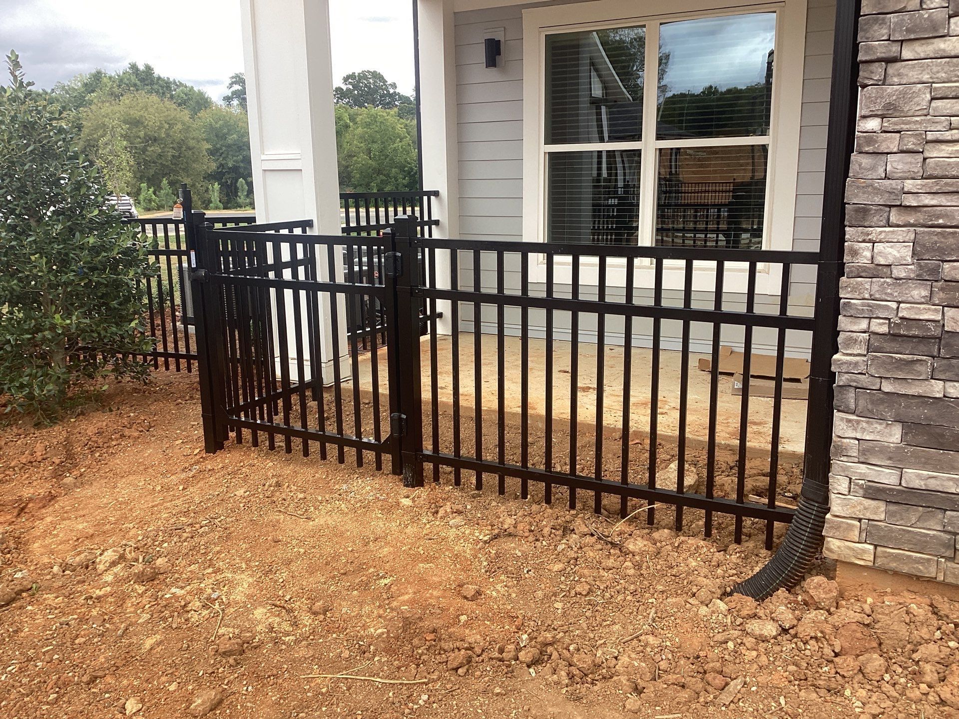 Black metal fence surrounding a porch area with a window. Dry dirt.
