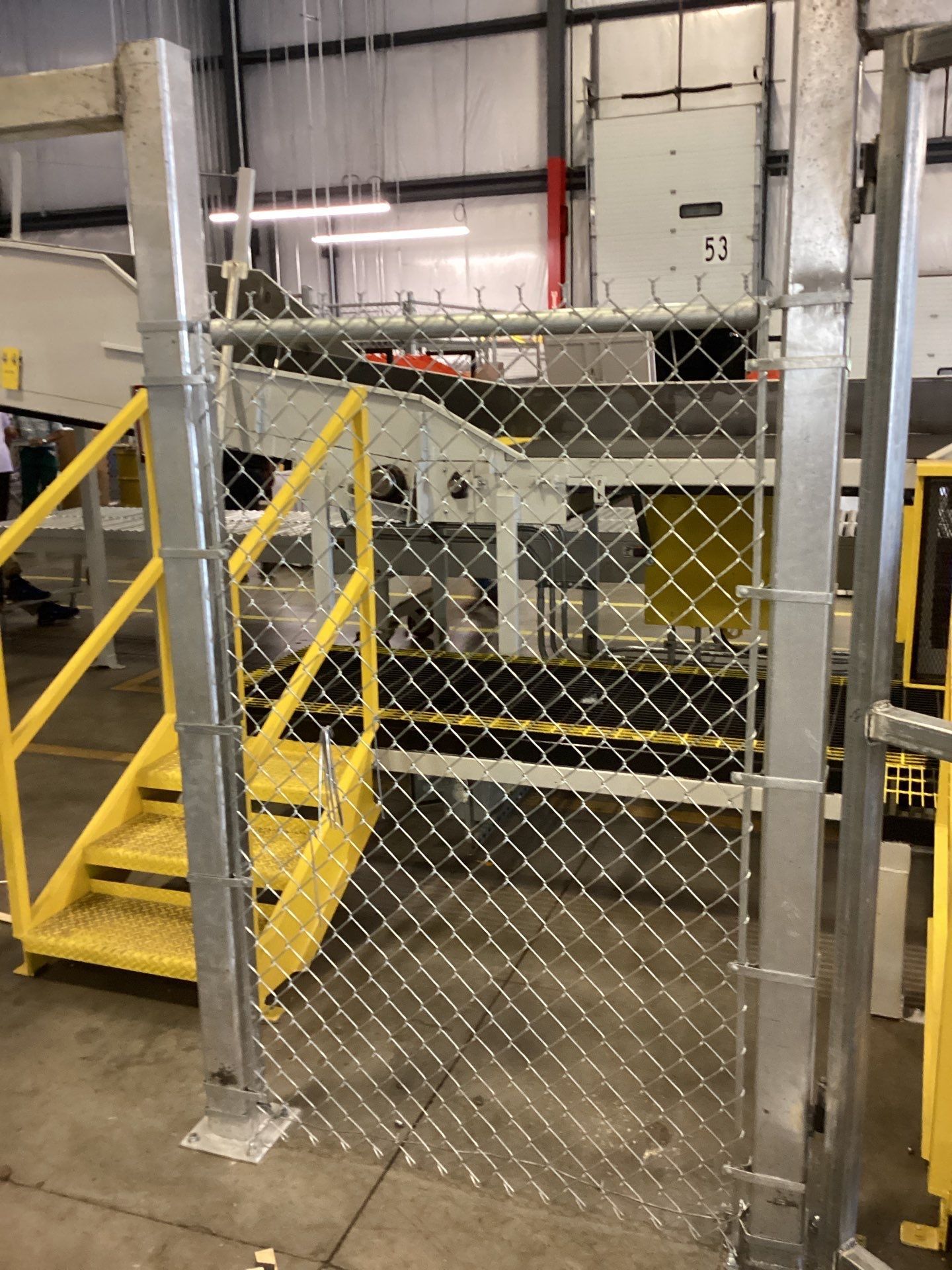 Chain-link fence gate with yellow stairs leading up to industrial machinery.