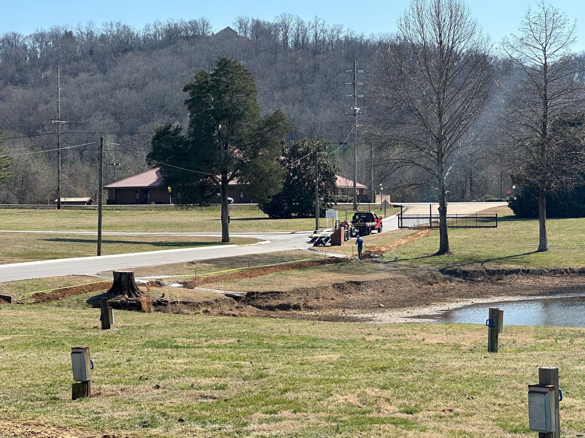 Park scene with a building, pond, trees, and vehicles; sunny day.