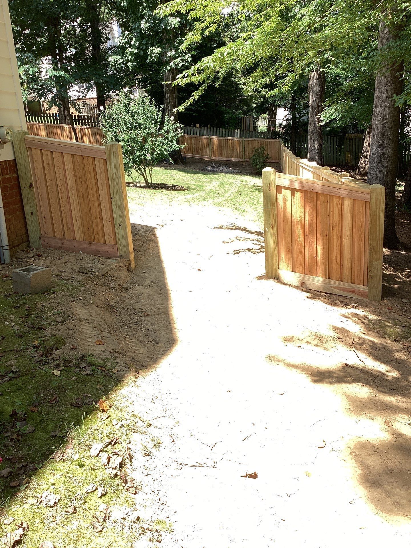 A dirt pathway leads between two new wooden fences in a backyard with trees.