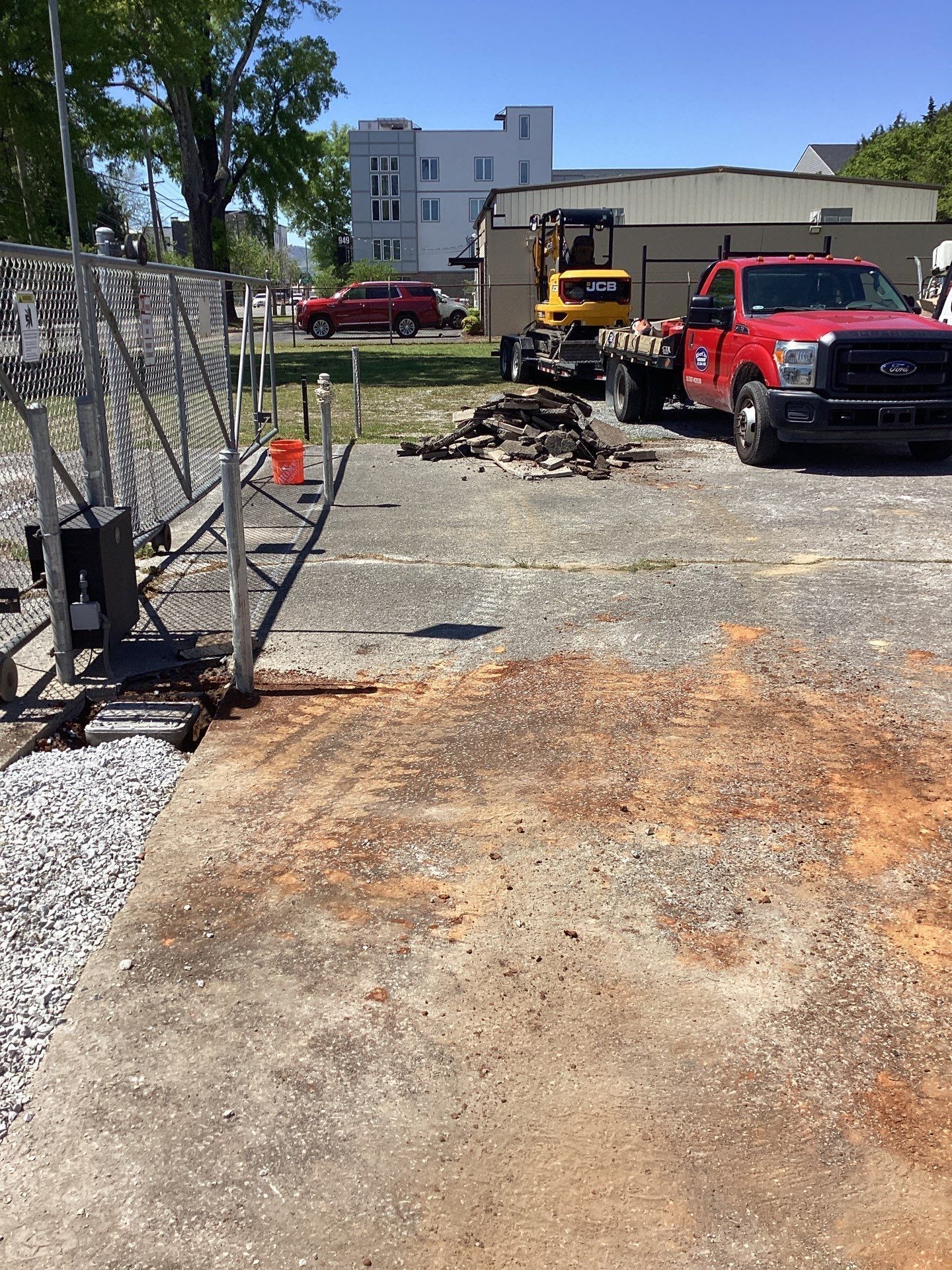 A construction site with a red truck, excavator, and a gate on a gravel surface.