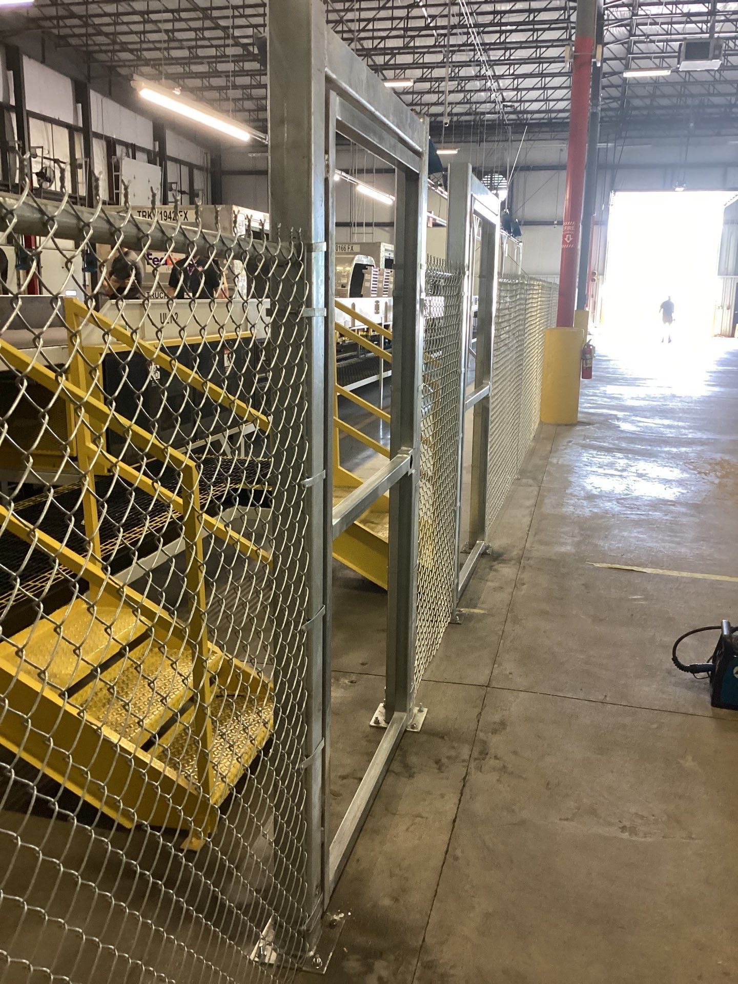 Chain-link fence with yellow stairs, industrial setting. Open doorway with person visible.