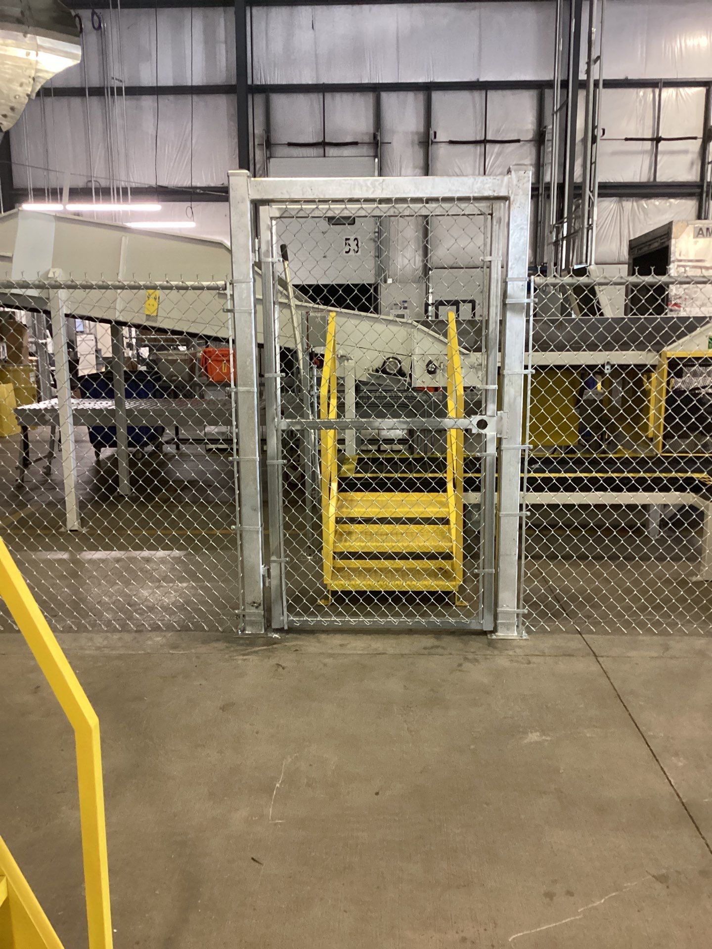 Yellow metal stairs within a chain link fence, likely for accessing equipment in an industrial setting.