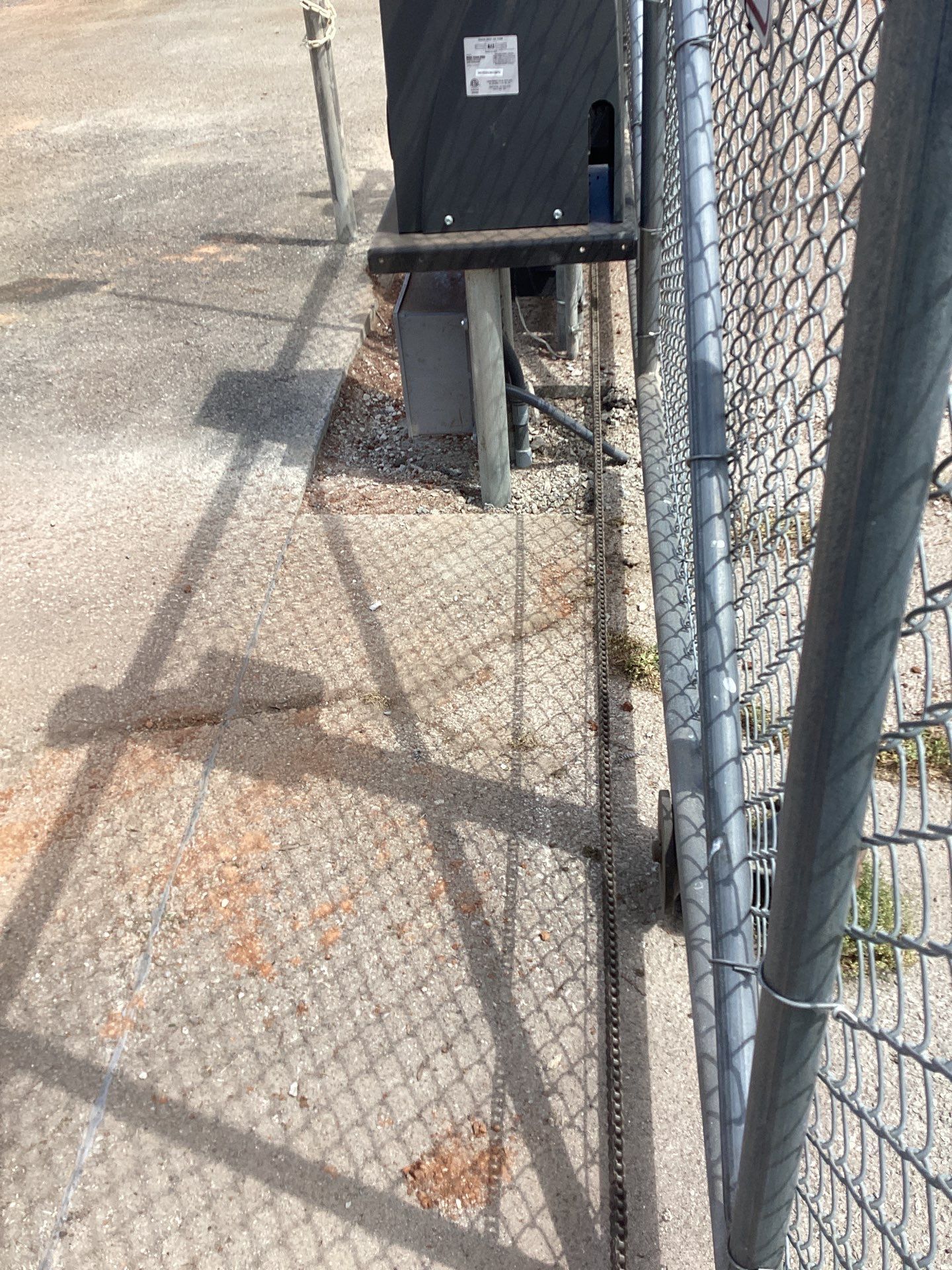 Chain-link fence next to a paved surface. A black box and metal pole are to the left.