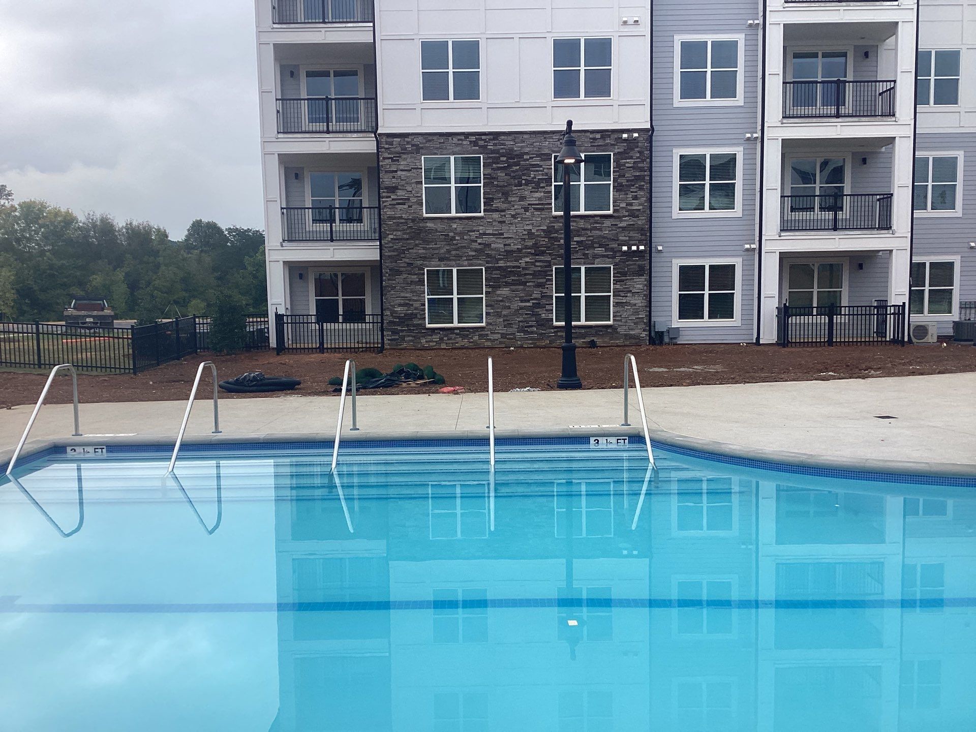 Pool with handrails in front of a multi-story building with balconies.